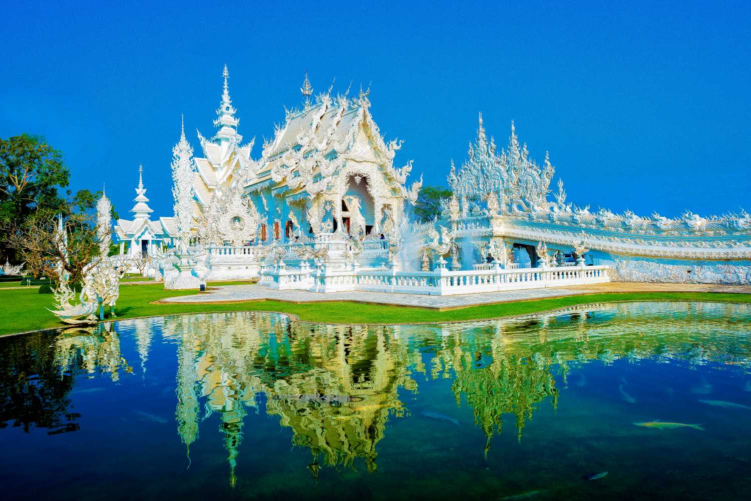 Wat Rong Khun White Temple Chiang Rai Thailand 2026 — mirror-glass encrusted white temple glistening in morning sunlight over reflective moat