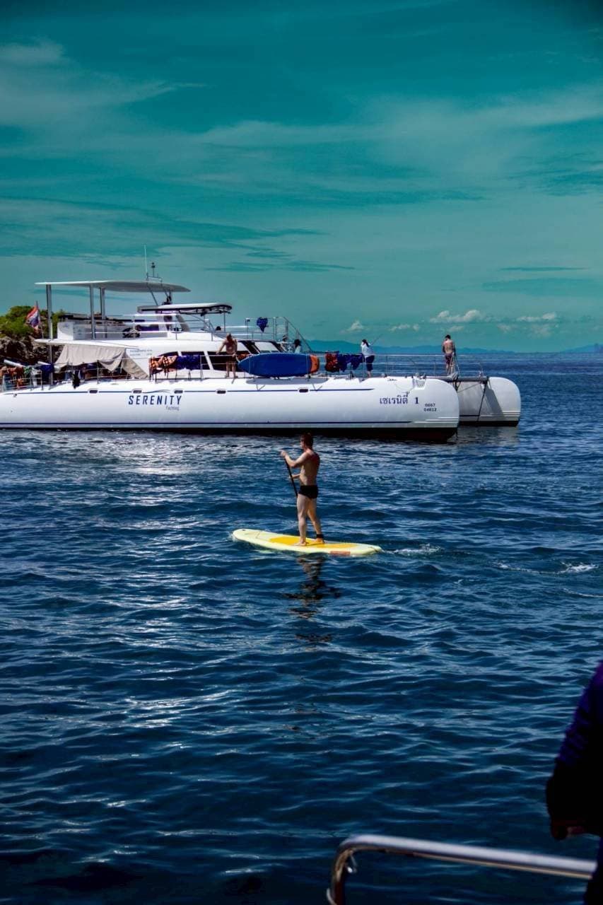 Paddleboarding beside the Serenity catamaran on the Pattaya 3 island yacht tour