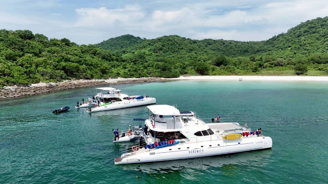 Two Serenity catamarans anchored in a turquoise bay beside an island beach near Pattaya