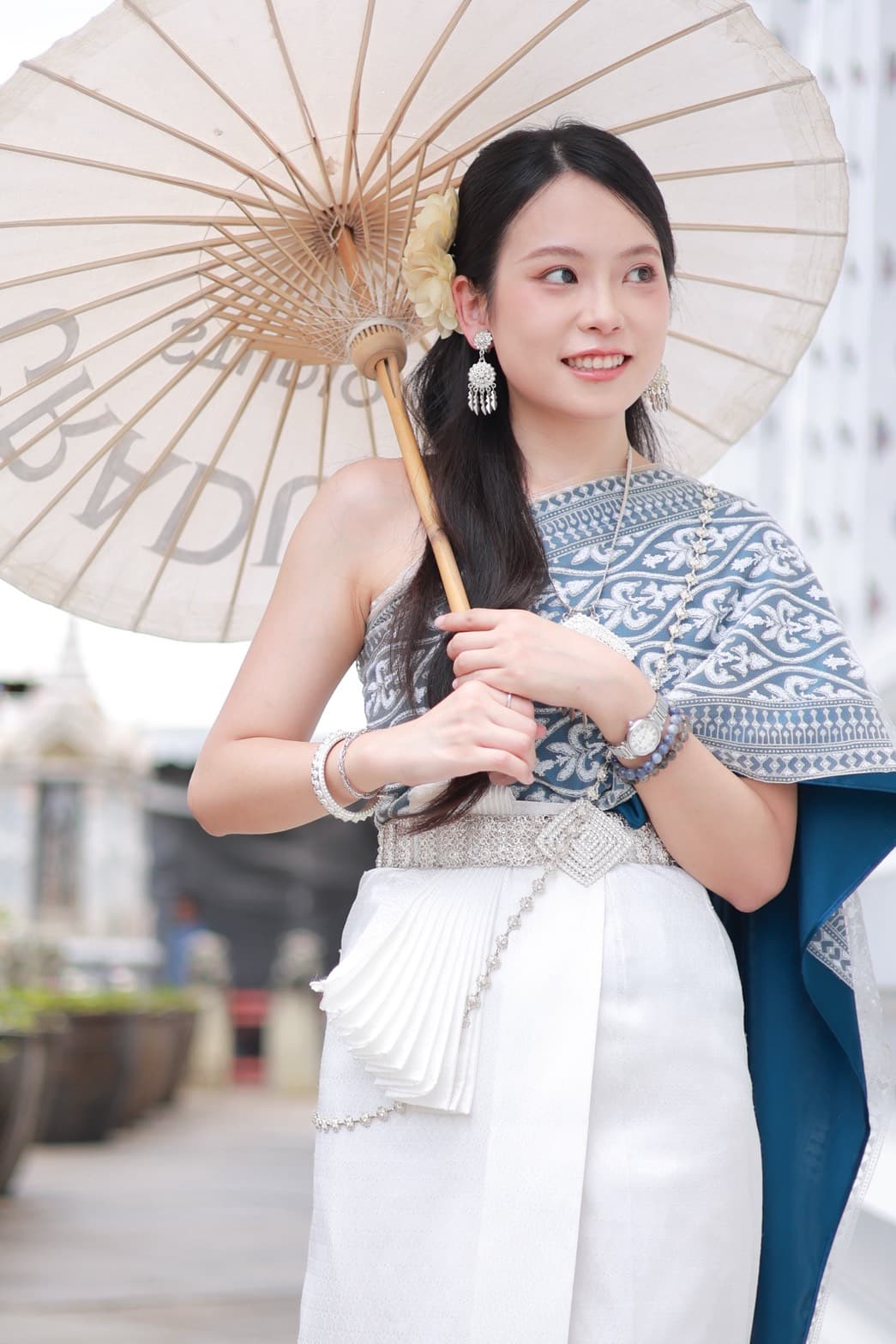 Woman in blue and white Thai traditional dress holding a paper parasol at Wat Arun Bangkok
