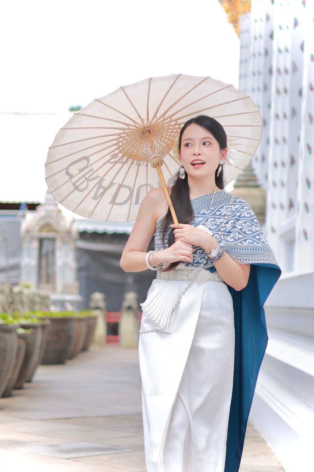 Woman in blue and white Thai traditional costume with paper parasol on the terrace at Wat Arun Bangkok