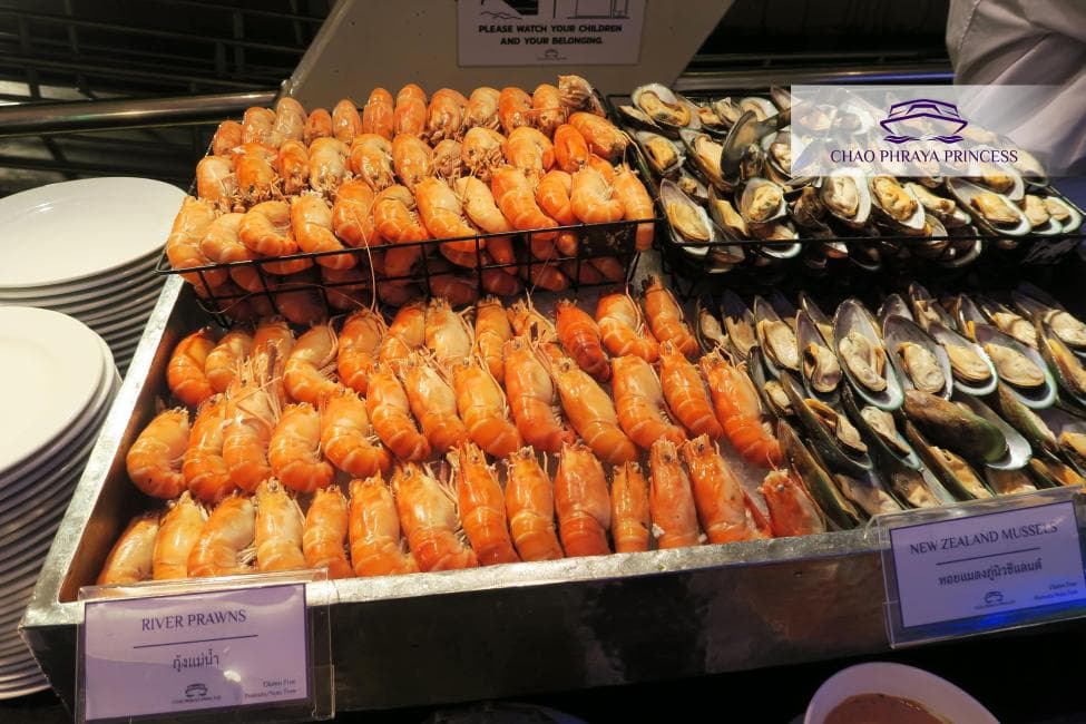 A Chao Phraya dinner cruise buffet with grilled river prawns, salmon sashimi and sushi — the seafood spread common across the Bangkok dinner cruise fleet