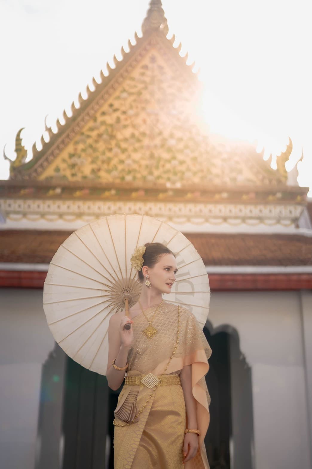 Western visitor in gold Thai traditional dress with paper parasol at Wat Arun Bangkok