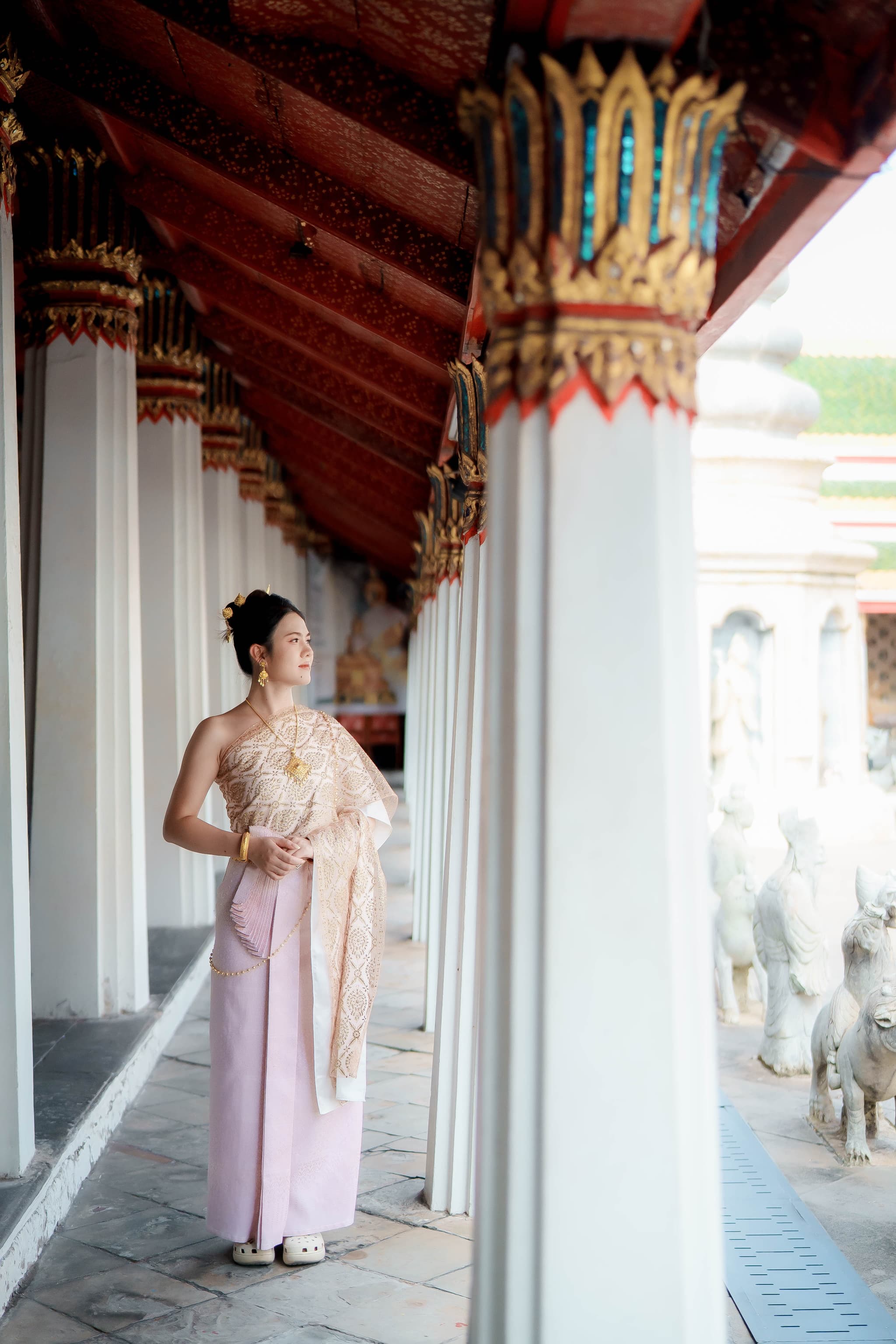 Woman in pink and gold Thai traditional dress in the colonnade at Wat Arun Bangkok